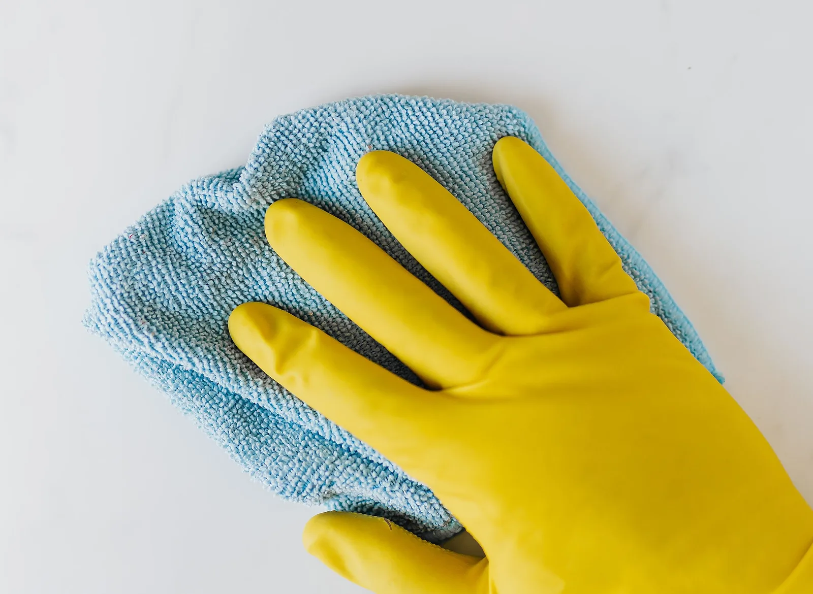 A gloved hand wiping a white surface with a blue microfibre cloth